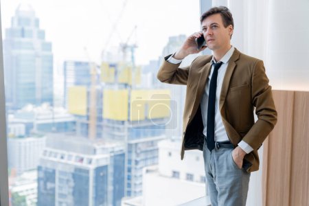 Photo for Portrait of professional businessman standing near window while phone calling. Smart executive manager thinking about business plan, project, idea while calling manager. Skyscraper view. Ornamented. - Royalty Free Image