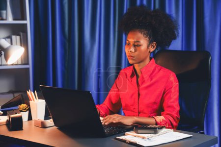 Téléchargez les photos : Femme d'affaires africaine ou blogueuse portant une chemise rose avec un visage sérieux, regardant et se concentrant sur un ordinateur portable à l'écran avec un projet de lutte. Concept d'expression stressante au travail depuis la maison. Tastemaker. - en image libre de droit