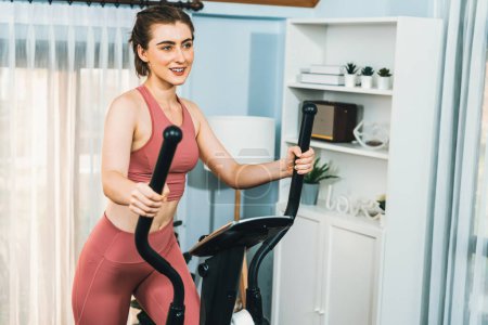 Photo for Athletic and sporty woman running on elliptical running machine during home body workout exercise session for fit physique and healthy sport lifestyle at home. Gaiety home exercise workout training. - Royalty Free Image