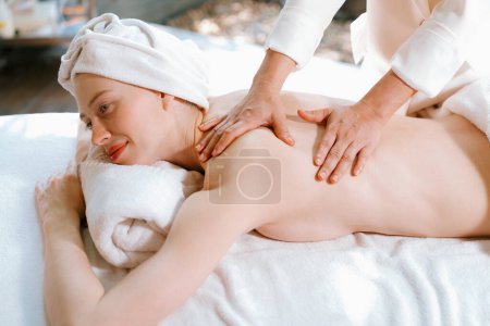 Téléchargez les photos : Belle jeune femme se couche sur un lit de spa lors d'un massage du dos. Belle femme caucasienne ayant massage du dos au salon de spa traditionnel, salle de spa. Concept relaxant et sain Tranquillité. - en image libre de droit