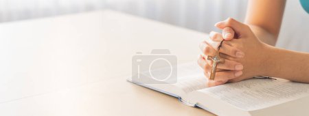 Photo for Cropped image of female reading a bible book while holding cross at wooden table with blurring background. Concept of hope, religion, faith, christianity and god blessing. Warm. Burgeoning. - Royalty Free Image