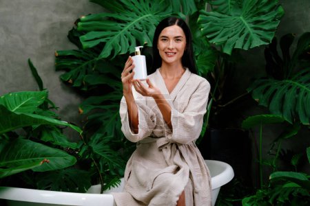 Photo for Tropical and exotic spa garden with bathtub in modern hotel or resort with woman in bathrobe holding beauty skincare product while enjoying leisure lush with greenery foliage background. Blithe - Royalty Free Image