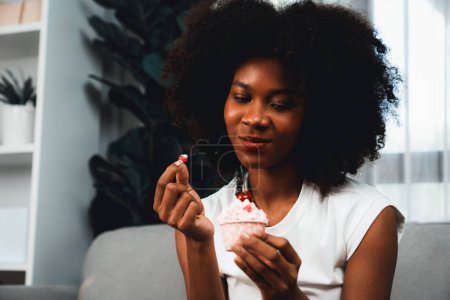 Photo for Portrait of beautiful young African blogger tasting piece of cherry cake in concept special cuisine. Presenting cute cupcake decorate fruit for content creating on social media. Tastemaker. - Royalty Free Image