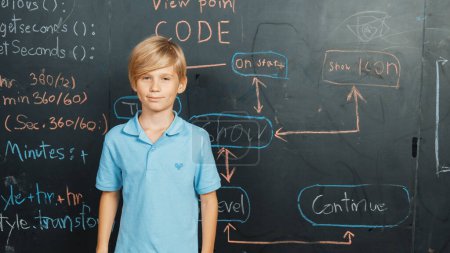 Photo for Boy standing at blackboard with engineering prompt written while looking at camera. Caucasian student planing a project by using coding and programing system in STEM technology classroom. Erudition. - Royalty Free Image