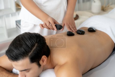 Photo for Hot stone massage at spa salon in luxury resort with day light serenity ambient, blissful man customer enjoying spa basalt stone massage glide over body with soothing warmth. Quiescent - Royalty Free Image