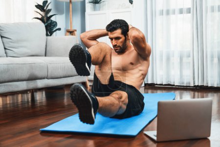 Photo for Athletic and sporty man doing crunch on fitness mat while follow online home workout exercise instruction for fit physique and healthy sport lifestyle at home. Online gaiety home exercise video. - Royalty Free Image