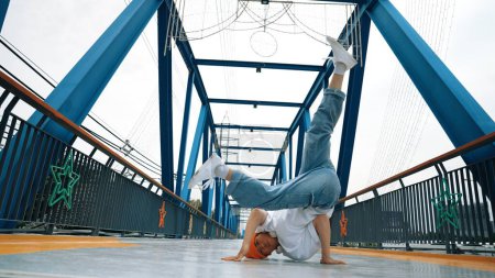 Photo for Professional break dancer perform street dance footstep at bridge. Asian hipster wear headphone while doing freeze pose. Break dancer, street dancer freestyle concept. Outdoor sport 2024. Sprightly. - Royalty Free Image