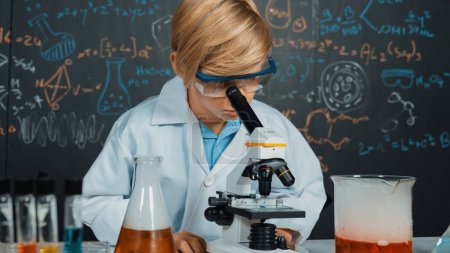 Photo for Smart boy using microscope analysis sample at science laboratory in STEM science class or chemistry lesson. Happy caucasian student looking under scope to inspect chemical liquid in tubes. Erudition. - Royalty Free Image