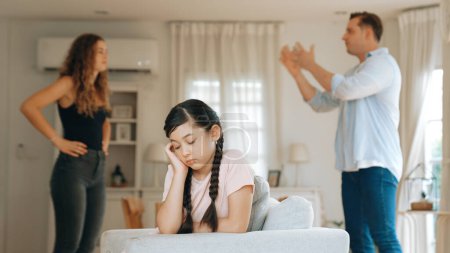 Photo for Annoyed and unhappy young girl sitting on sofa trapped in middle of tension by her parent argument in living room. Unhealthy domestic lifestyle and traumatic childhood develop to depression Synchronos - Royalty Free Image