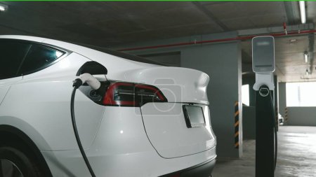Photo for EV electric car recharge at shopping center multistorey indoor parking lot charging in downtown city showing urban sustainability green clean rechargeable energy lifestyle of electric vehicle innards - Royalty Free Image