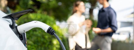 Photo for Young couple recharge electric car battery from charging station in green city park in springtime. Rechargeable EV car for sustainable environmental friendly urban travel lifestyle. Panorama Expedient - Royalty Free Image