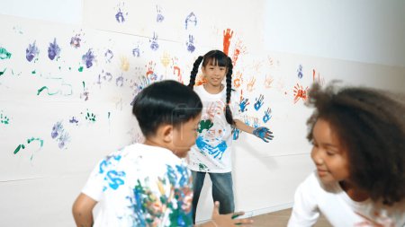 Photo for Playful children playing and running with colorful stained hand in front of white background. Funny happy multicultural students enjoy attending in art lesson. Creative activity concept. Erudition. - Royalty Free Image