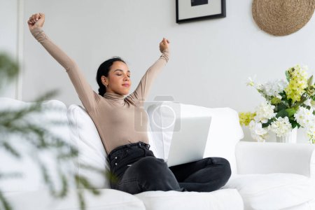 Foto de Joven mujer afroamericana estirando los brazos para una relajación crucial en casa. La mujer feliz pasar el fin de semana mañana en la sala de estar. - Imagen libre de derechos