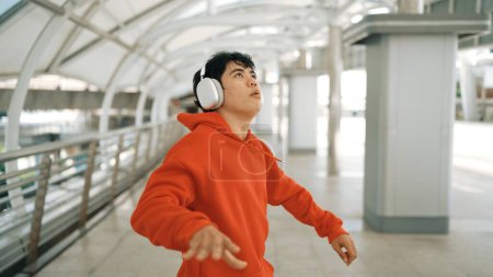 Photo for Skilled hipster listening music from headphone while moving and waving hand with blurring background. Stylish street dancer walking at corridor or perform freestyle dance. Modern lifestyle. Sprightly. - Royalty Free Image