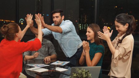Photo for Group of businesspeople clap hands and gives high five together to celebrate success project, good news. Business team applause to celebrate promotion at meeting table at night office. Tracery - Royalty Free Image