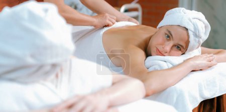 Téléchargez les photos : Portrait de deux jolies jeunes femmes avec une belle peau en serviette blanche se faisant masser le dos par un masseur professionnel au salon de spa traditionnel. Beauté et santé. Tranquillité. - en image libre de droit