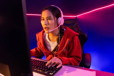 Photo for Host channel of beautiful Asian girl streamer concentrating online game wearing headphones pastel color talking with viewers media online. Esport skilled team players in neon blue room. Stratagem. - Royalty Free Image