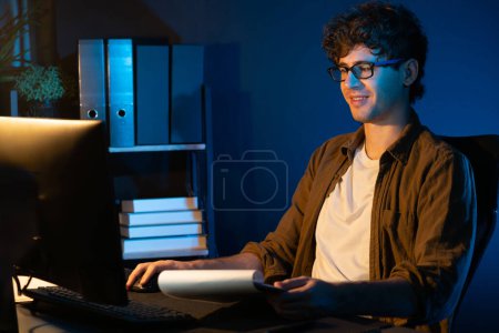 Photo for Young businessman reading design thinking on paper for new project surround work desk at neon light modern office. Thinking new next job sketching on notebook before sending present via email. Gusher. - Royalty Free Image