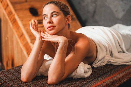 Téléchargez les photos : Jolie jeune femme se trouve sur un lit de spa en face de l'armoire de sauna en bois. Attrayant relaxant femmes caucasiennes en serviette blanche en attente de massage du corps dans le salon de spa, salle de sauna.. - en image libre de droit