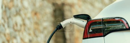 Photo for Panorama closeup EV charger handle plugged in or connect to electric car, recharging EV car battery with alternative and sustainable energy with zero CO2 emission for clean environment. Perpetual - Royalty Free Image
