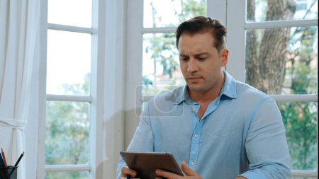 Téléchargez les photos : Homme d'affaires luttent pour résoudre le problème de travail de la maison en utilisant un ordinateur portable, assis sur son bureau au bureau à la maison avec l'expression stressée et frustrée, en essayant de trouver une solution pour le problème. Synchronos - en image libre de droit
