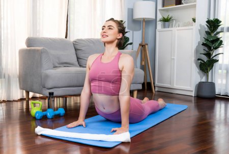 Photo for Flexible and dexterity woman in sportswear doing yoga position in meditation posture on exercising mat at home. Healthy gaiety home yoga lifestyle with peaceful mind and serenity. - Royalty Free Image