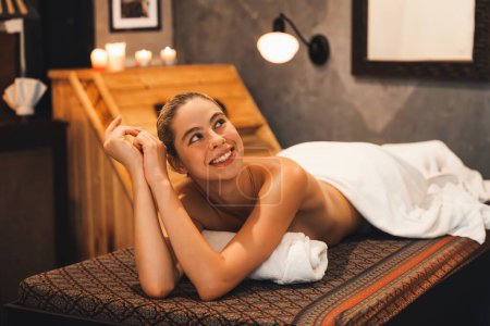 Portrait de belle femme caucasienne en serviette blanche femme se trouve sur un lit de spa en face de l'armoire de sauna en bois chaud avec détente et tranquillité au salon de spa. Ferme là. Une vue latérale. Tranquillité.