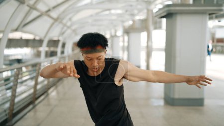 Photo for Smart handsome dancer moving hands while dance to hip hop music. Professional asian hipster wearing headphone while walking along the corridor with blurring background. Outdoor sport 2024. Sprightly. - Royalty Free Image