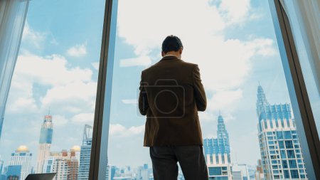Photo for Back view ambitious businessman standing in ornamented office gazing out window to cityscape skyline. Determination and business ambition drive business career toward to bright future - Royalty Free Image