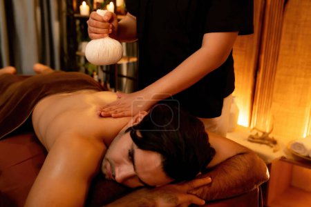 Photo for Caucasian man customer enjoying relaxing anti-stress spa massage and pampering with beauty skin recreation leisure in warm candle lighting ambient salon spa at luxury resort or hotel. Quiescent - Royalty Free Image