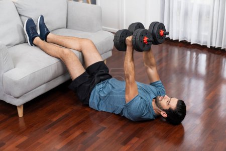 Photo for Athletic body and active sporty man using furniture for effective targeting muscle gain with weight lifting dumbbell exercise at gaiety home as concept of healthy fit body home workout lifestyle. - Royalty Free Image