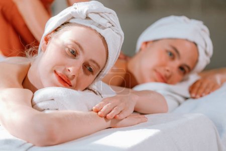 Téléchargez les photos : Un couple de belle jeune femme avec serviette blanche se trouvent sur un lit spa confortable pendant recevoir massage du corps relaxant par masseur professionnel entouré au salon de spa. Fond gris. Tranquillité. - en image libre de droit