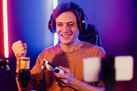 Photo for Enjoy smart gaming streamer with control joystick, playing game online of live streaming by smartphone rec with team skilled players on computer at modern technology cyber neon light room. Pecuniary. - Royalty Free Image