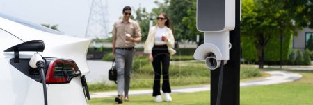 Photo for Young couple with coffee recharge EV car battery at charging station connect to electrical industrial power grid. Couple with shopping and travel using eco electric car lifestyle.Panorama Expedient - Royalty Free Image