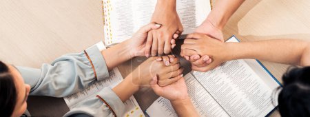 Imagen recortada de la diversidad de la mano de la gente rezando juntos en la iglesia de madera en el libro de la Biblia mientras se toman de la mano junto con creer. Concepto de fe, concepto de bendición de Dios. Vista superior. Florecimiento.