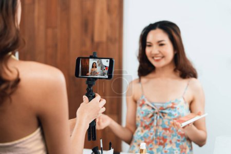 Téléchargez les photos : Asian Woman influenceur shoot live streaming vlog video review makeup uttermost réseaux sociaux ou blog. Heureuse jeune fille avec éclairage de studio cosmétique pour la diffusion de session d'enregistrement marketing en ligne - en image libre de droit