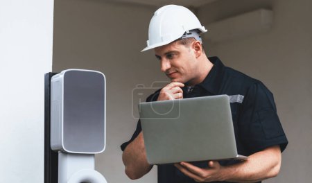 Photo for Qualified technician working on home EV charging station installation, making troubleshooting and configuration setup on charging system with laptop for EV at home. Synchronos - Royalty Free Image