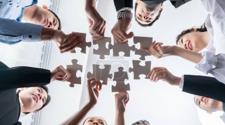 Téléchargez les photos : Des hommes d'affaires multiethniques tenant des pièces de puzzle et les fusionnant en tant que solution efficace pour résoudre le travail d'équipe, la vision partagée et l'objectif commun combinant divers talents. En dessous. Habillement - en image libre de droit