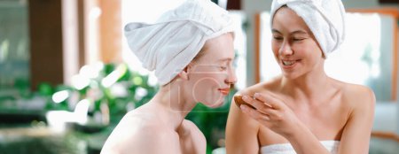 Photo for Couple of beautiful woman interested in homemade facial masks while sitting at spa salon. Attractive woman in white towel enjoy herbal masks with her friend surrounded by nature. Tranquility. - Royalty Free Image