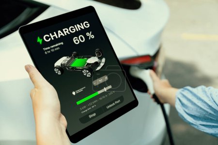 Photo for Hand insert EV charger plug into electric vehicle to recharge EV car, battery status display on tablet EV application. Future alternative clean and sustainable energy for transportation. Perpetual - Royalty Free Image