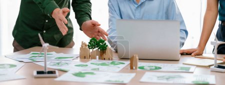 Photo for Cropped image of skilled businessman presented eco-friendly house project to general manager at meeting table with wooden block, windmill model and environmental document scatter around. Delineation. - Royalty Free Image