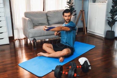 Photo for Athletic and sporty man pulling resistance band exercise during home workout exercise session for fit physique and healthy sport lifestyle at home. Gaiety home exercise workout training concept. - Royalty Free Image