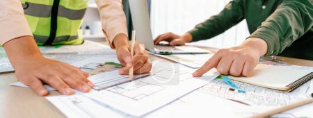Photo for Professional engineer team discussion about house design on meeting table with architectural equipment and blueprint scatter around at modern office. Focus on hand. Closeup. Delineation. - Royalty Free Image