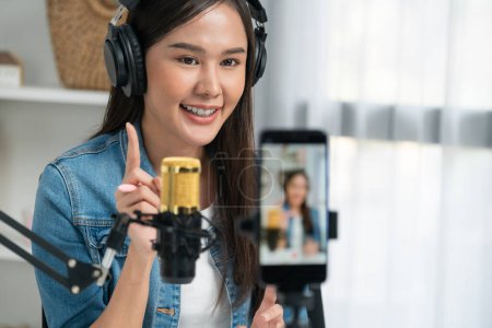 Photo for Host channel Asian influencer talking in broadcast wearing headsets on social media live on smartphone recording online, greeting listeners with coaching life or business at modern studio. Stratagem. - Royalty Free Image