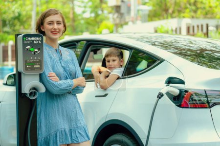 Photo for Environmental awareness family with eco-friendly electric car recharging battery from home EV charging station with little boy inside the car. Rechargeable and EV car technology. Perpetual - Royalty Free Image