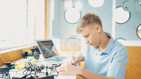 Photo for Caucasian boy fixing main board while study construction by using laptop analysis data. Young technician repairing and learning about using industrial structure at STEM technology class. Edification. - Royalty Free Image