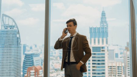 Photo for Businessman standing in ornamented office talking on phone with college on cityscape skyline window background. Determination and ambition drive business career toward to bright future - Royalty Free Image