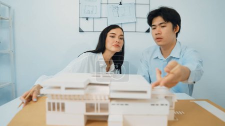 Photo for Closeup of skilled architecture engineer team measure and decide house model while working together and discussing about house structure at meeting room with blueprint placed behind. Immaculate. - Royalty Free Image