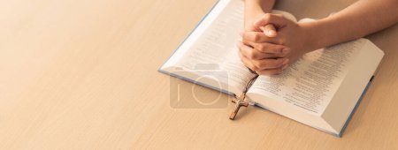 Photo for Cropped image of praying male hand holding cross on holy bible book at wooden table. Top view. Concept of hope, religion, faith, christianity and god blessing. Warm and brown background Burgeoning. - Royalty Free Image