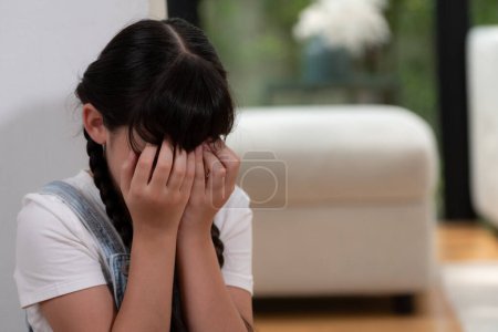 Photo for Sad little girl sitting alone in living room crying, feeling lonely. Young girl experiencing social isolation punishment or neglect from parent led to anxiety and traumatic in childhood. Synchronos - Royalty Free Image